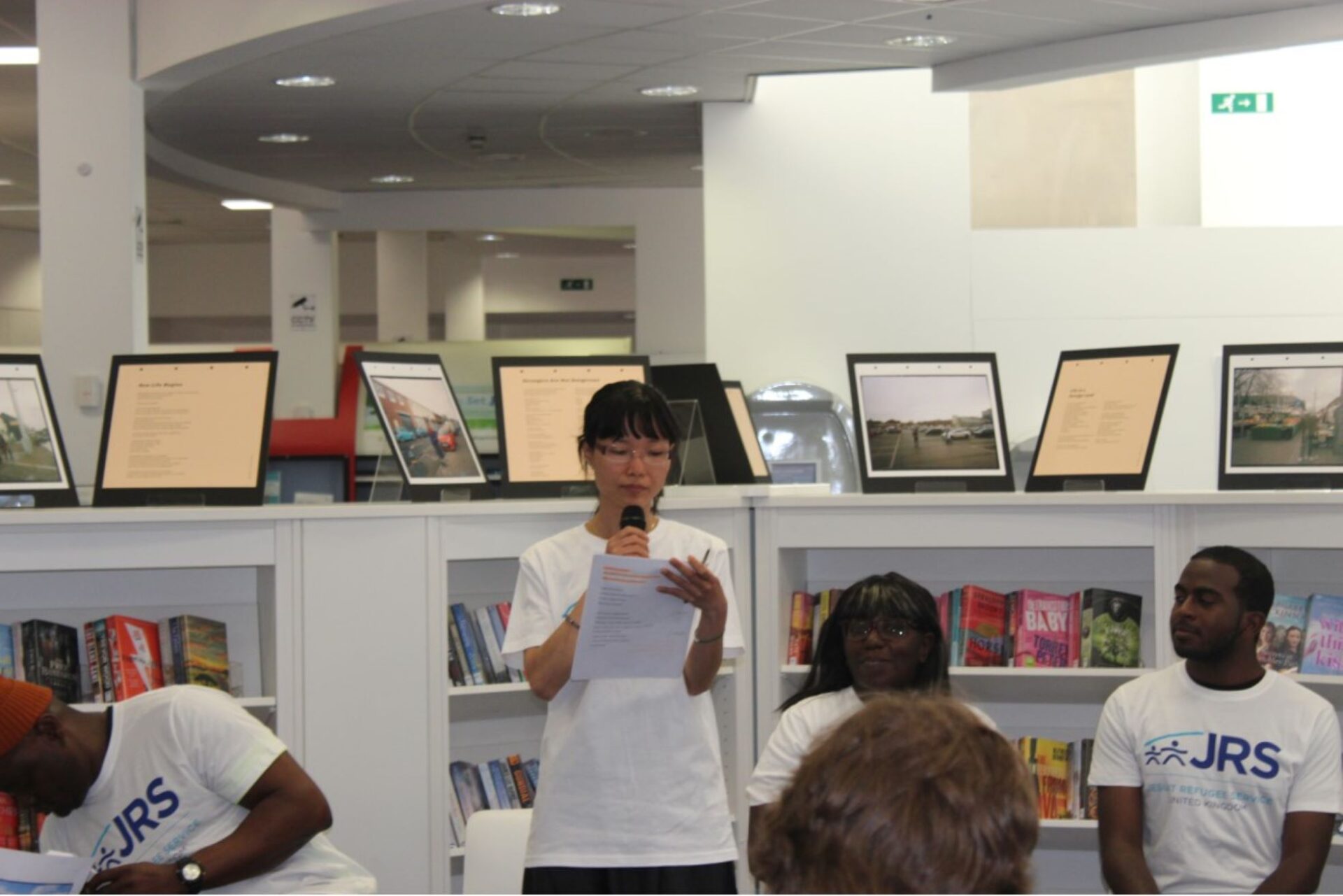 Woman reading from a piece of paper with a display of images and text on a cabinet behind her