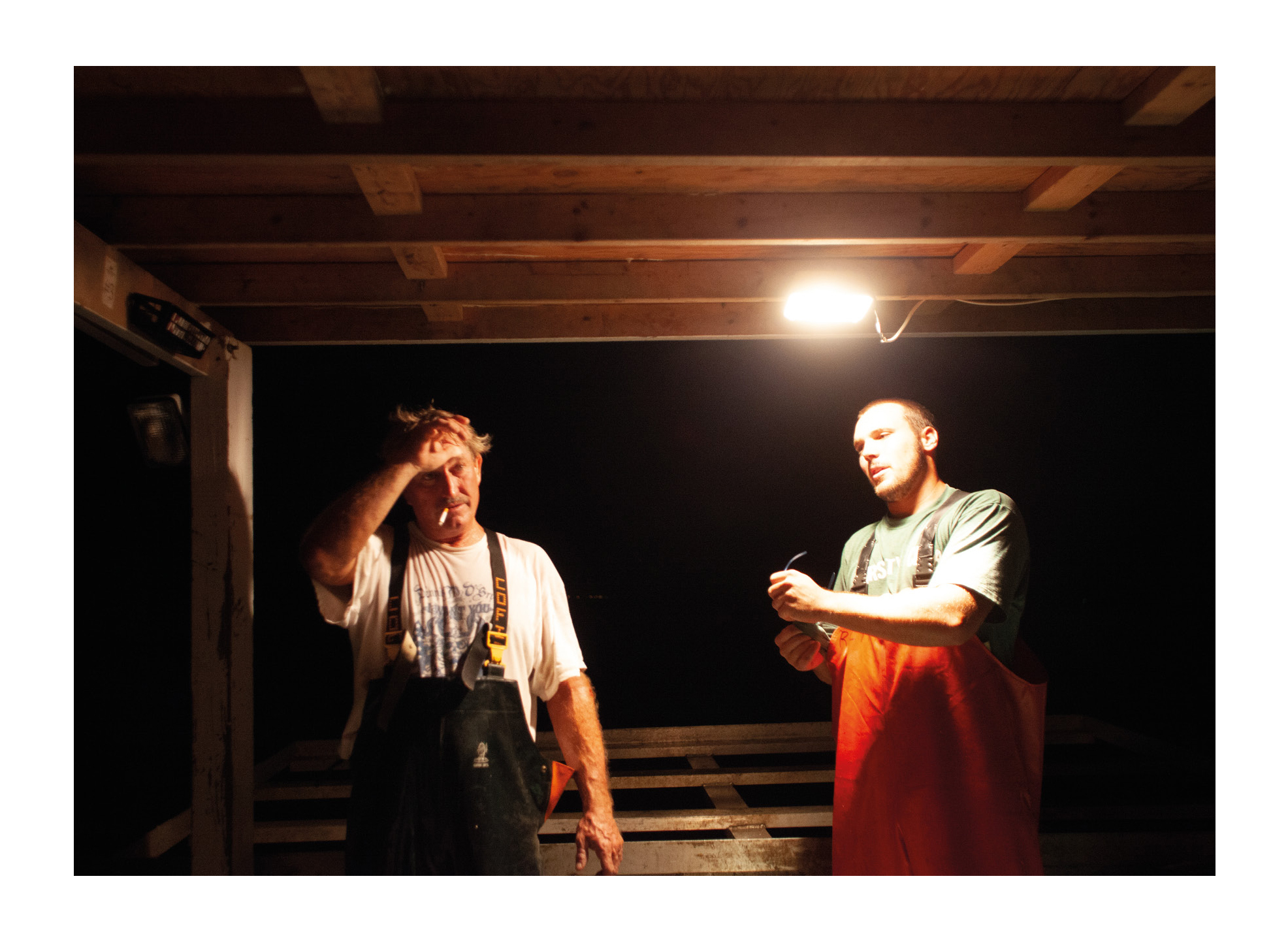 Photograph from Tangier Island photography zine showing two watermen working on their boat at night